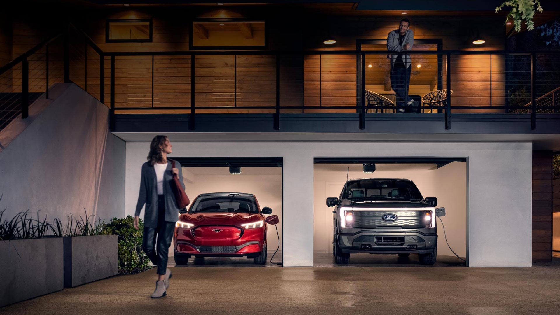 Woman walking out from home garage with a 2024 Mustang® Mach-E and Ford Lightning® truck in plugged-in and charging | Bergstrom Ford of Green Bay in Green Bay WI